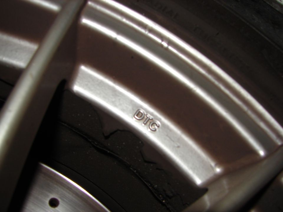 Close-up of a silver car wheel showing the marking "DTC" and part of a tire