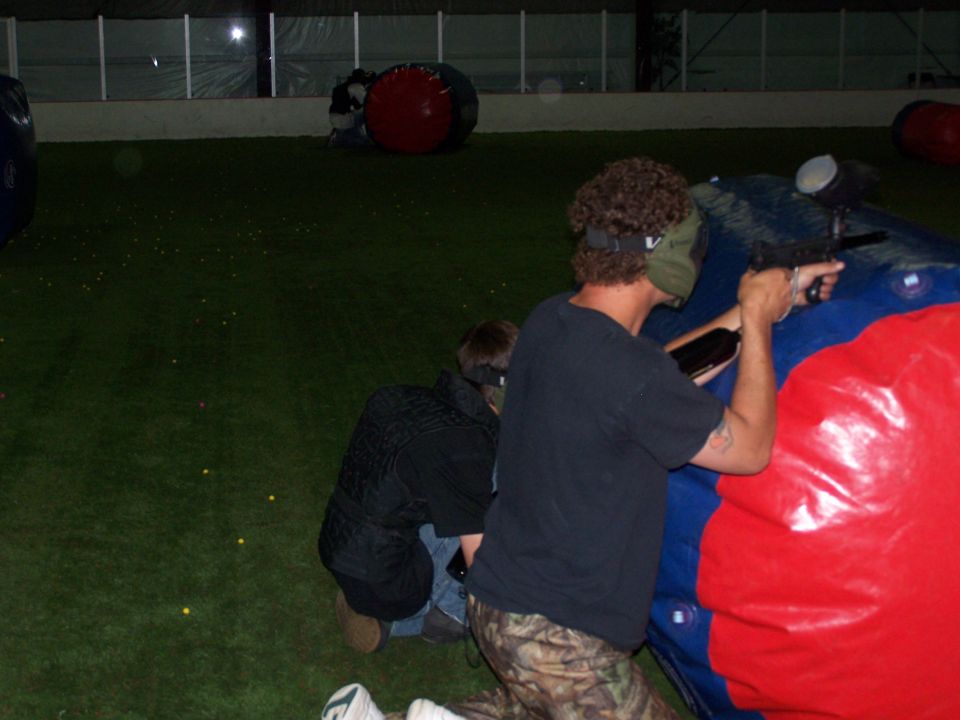 People playing paintball indoors on a turf field with inflatable barriers