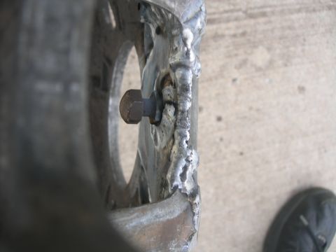 1984 Ford Bronco - A close-up view of a heavily modified metal component, possibly a vehicle part, with visible bolt and rough welding.