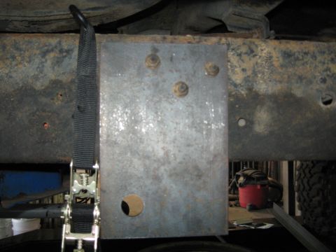 1978 Ford Bronco - A metal plate is bolted to the underside of a vehicle's frame, secured by a ratchet strap.