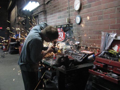 1978 Ford Bronco - A worker uses an angle grinder, creating a shower of sparks in a workshop setting.