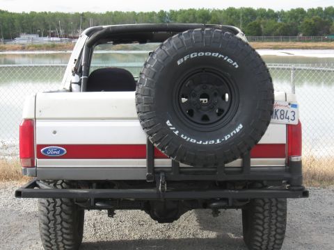 1991 Ford Bronco - The rear of a white Ford Bronco is shown with a spare tire, a red stripe, and a California license plate.