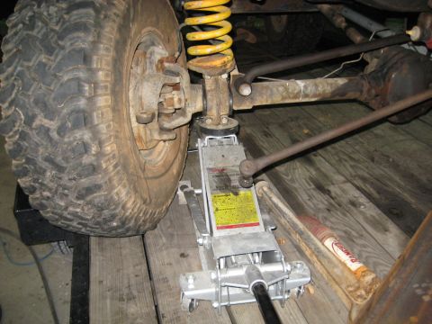 1978 Ford Bronco - A hydraulic jack is positioned under the axle of a vehicle, supporting the suspension system.