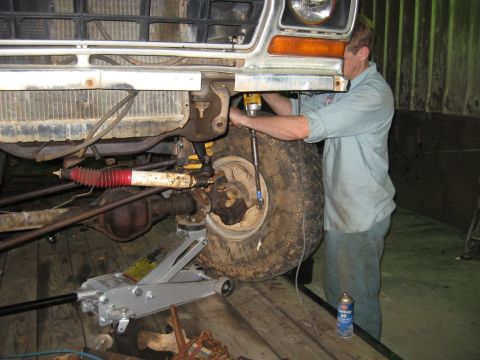 1978 Ford Bronco - A mechanic works on the front wheel of a 1978 Ford Bronco, which is supported by a jack.