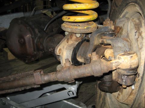 1978 Ford Bronco - Close-up view of the front axle and suspension system, including a yellow coil spring and various linkage components.