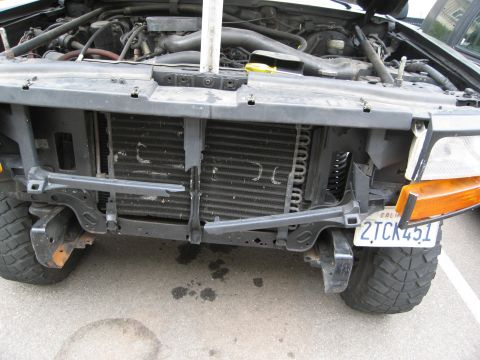 1986 Ford Bronco - The front end of a vehicle is visible with the hood open, revealing the engine and a damaged radiator.