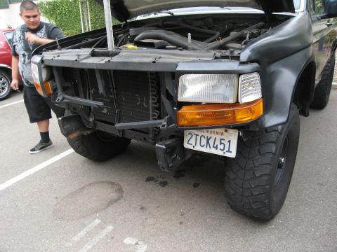 1986 Ford Bronco - The front end of a black Ford Bronco is shown with its hood open, revealing damage to the bumper and radiator area.