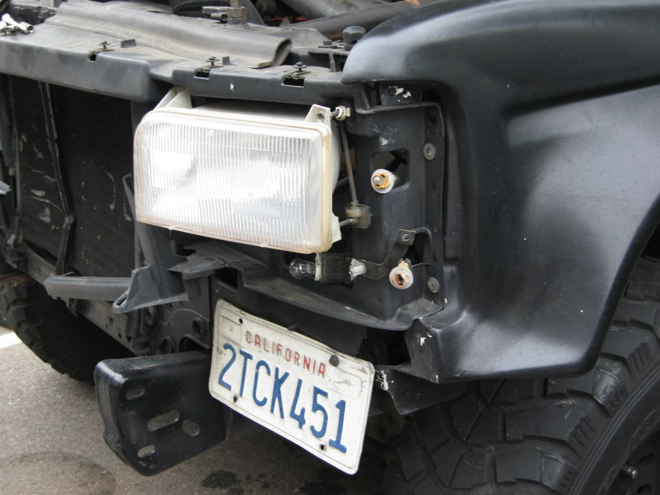 Black truck front end with missing headlight assembly and damaged bumper. California license plate 2TCK451 is visible