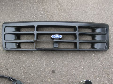 1986 Ford Bronco - A black Ford grille with the iconic blue oval badge is shown, displaying some damage on its lower section.