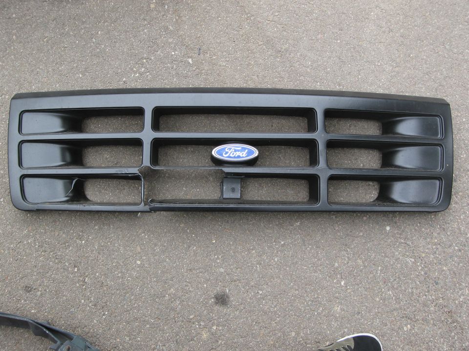 Black Ford grille with blue oval Ford badge. Some damage on lower left