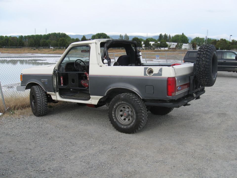 Two-tone Ford Bronco, doors off, spare tire on back. Other vehicle in background