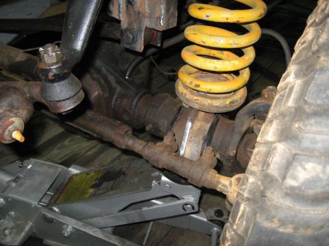 1978 Ford Bronco - This image shows the front suspension and steering components of a vehicle, including a yellow coil spring and a tire.
