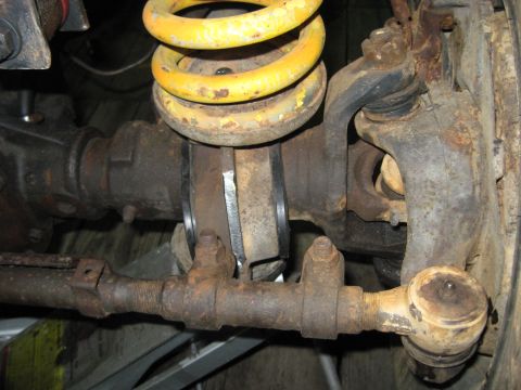 1978 Ford Bronco - Close-up of a heavily rusted vehicle's suspension system, including a yellow coil spring and tie rod ends.