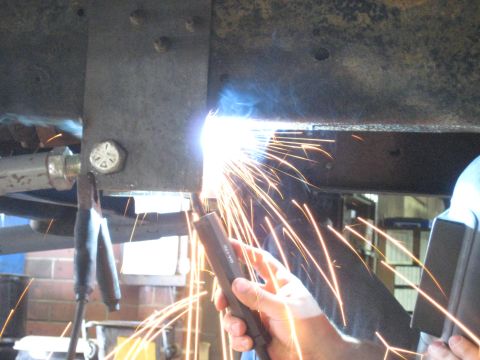 1978 Ford Bronco - A person welds a metal frame component on a vehicle chassis, with sparks flying.