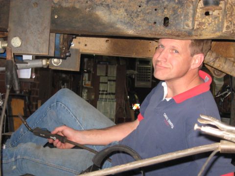 1978 Ford Bronco - A man welds a vehicle frame, with tools and parts visible in the workshop setting.