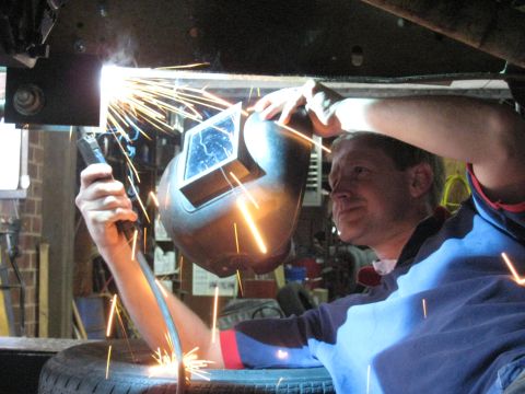 1978 Ford Bronco - Welding sparks fly as a mechanic works on the undercarriage of a vehicle.