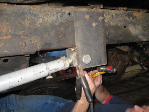 1978 Ford Bronco - A close-up shot shows a mechanic working on the undercarriage of a vehicle, modifying its frame with welding equipment.