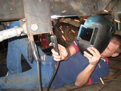1978 Ford Bronco - A person welds metal components beneath a vehicle, with sparks illuminating the scene.
