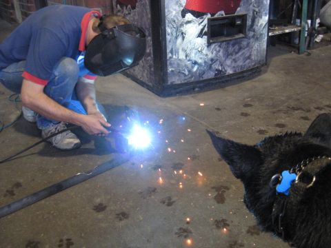 1978 Ford Bronco - A black dog observes a person welding a metal pipe in a workshop setting.