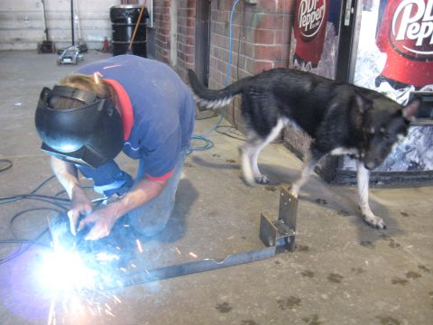 1978 Ford Bronco - A person is welding a metal object on the floor while a dog walks past, with a Dr Pepper machine visible in the background.