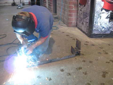 1978 Ford Bronco - A person welds a metal frame on a concrete floor marked with paw prints.