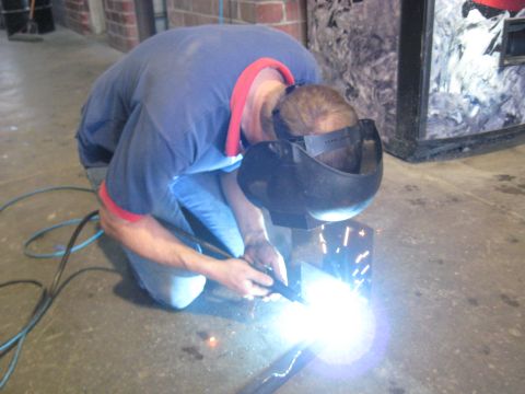 1978 Ford Bronco - A person wearing a welding mask and protective gear is kneeling and welding metal, creating bright sparks.