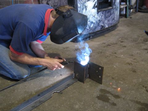 1978 Ford Bronco - A person wearing a welding mask and blue shirt welds metal components in a workshop setting.