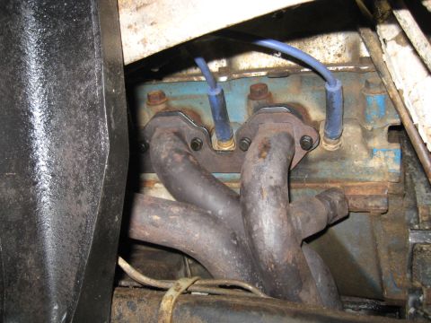 1978 Ford Bronco - Close-up view of an exhaust manifold and spark plug wires attached to a blue engine block, likely from an older vehicle.