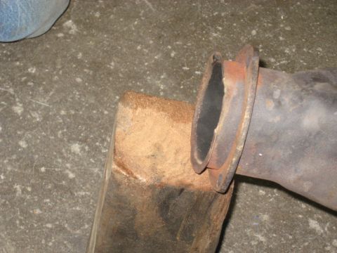 1978 Ford Bronco - Close-up of an exhaust pipe flange secured by a wooden block, suggesting a repair or maintenance activity.