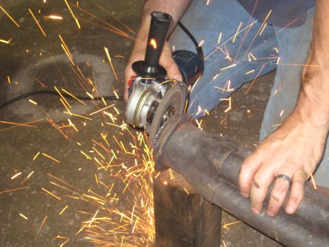 1978 Ford Bronco - A person uses an angle grinder to cut an exhaust pipe, creating a shower of sparks.