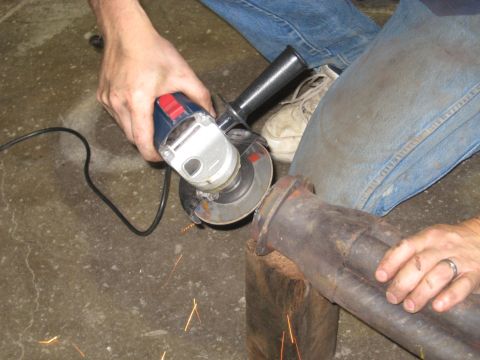1978 Ford Bronco - An exhaust pipe is being cut with an angle grinder, with sparks flying from the friction.
