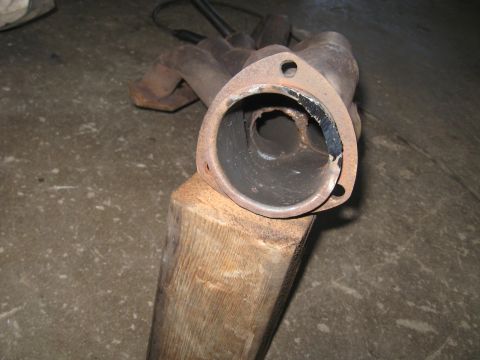 1978 Ford Bronco - A rusty exhaust manifold with a broken flange is shown, resting on a wooden block.