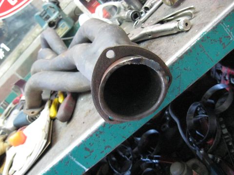1978 Ford Bronco - Close-up of an exhaust manifold, likely for an older vehicle, resting on a workbench.