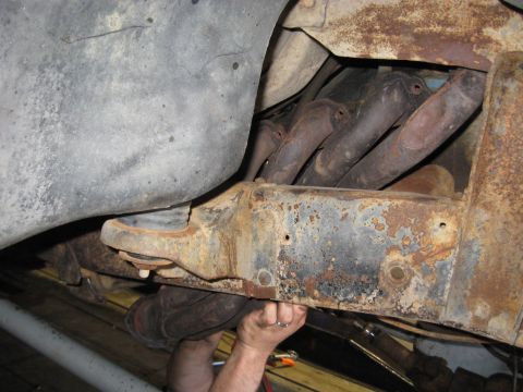 1978 Ford Bronco - Close-up view of a rusty vehicle frame and exhaust manifold, with hands working on the frame.