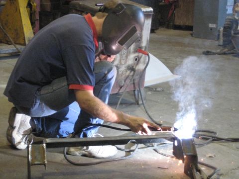 1978 Ford Bronco - A person welds metal components in a workshop environment, with visible sparks and smoke.