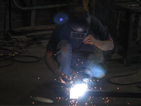 1978 Ford Bronco - A welder is crouched down, using a torch to create sparks while working on a metal piece.