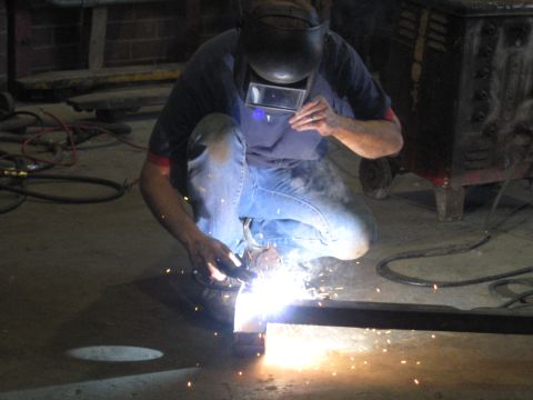 1978 Ford Bronco - Welding a metal beam in an indoor workshop setting with sparks flying.