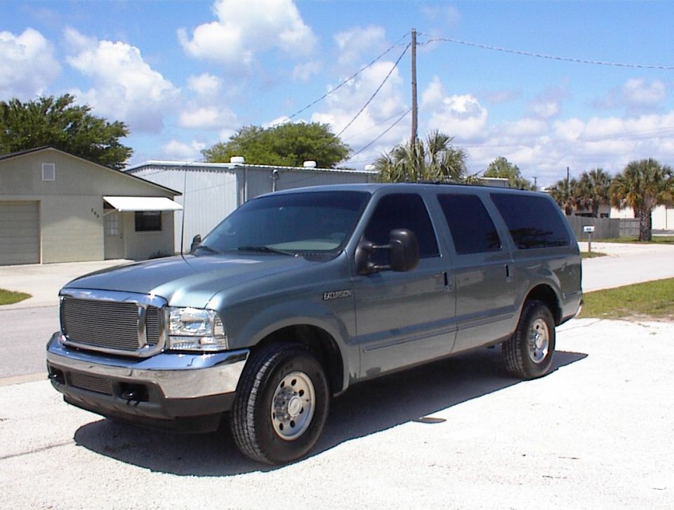 Teal-green Ford Excursion SUV, 3q front, chrome billet grille, on paved lot