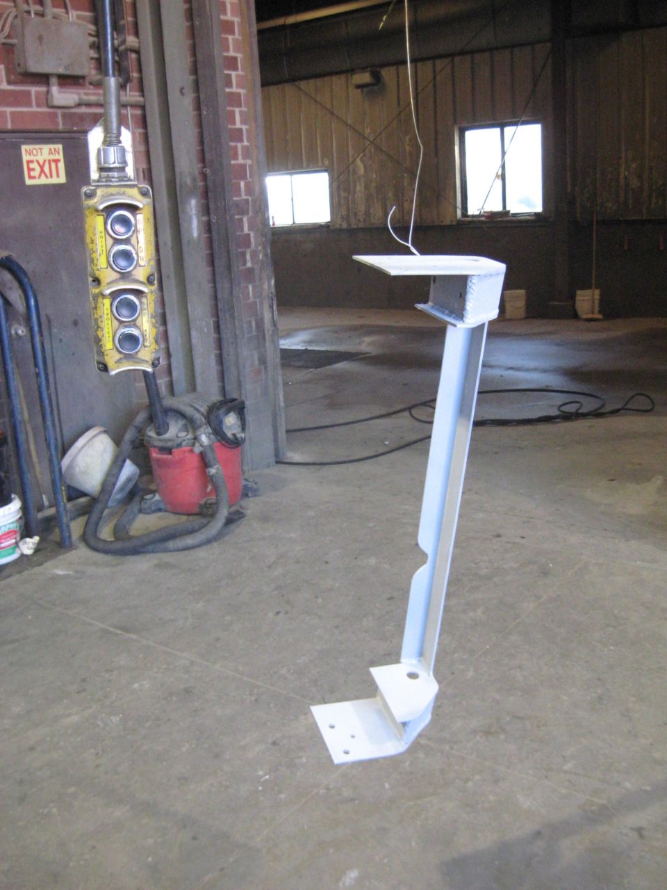 Painted metal bracket with a base plate and a horizontal shelf, in a workshop setting