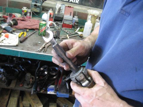 1978 Ford Bronco - A mechanic works with a tool on a workbench cluttered with tools and supplies.