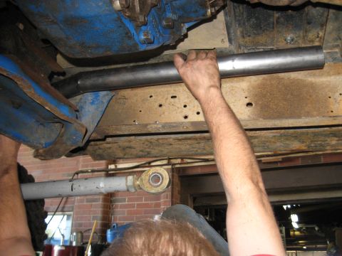 1978 Ford Bronco - A close-up view of a mechanic's hands working on the undercarriage of a vehicle, installing a new pipe.
