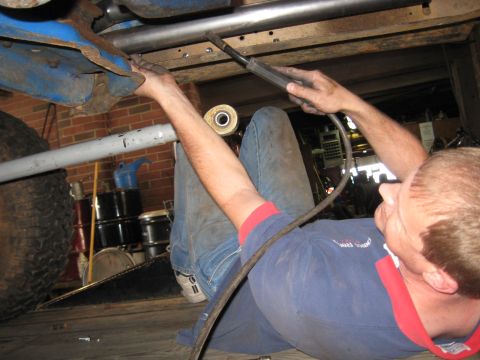 1978 Ford Bronco - Mechanic performing maintenance on the undercarriage of a vehicle in a garage setting.