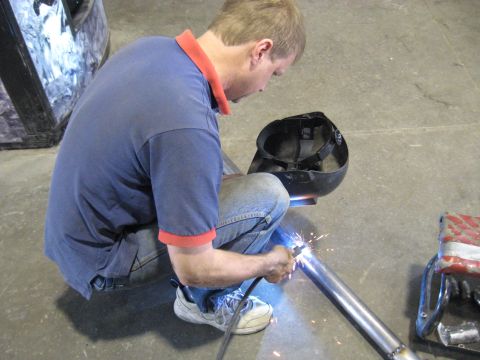 1978 Ford Bronco - A person is welding a metal pipe in an indoor setting, with sparks flying from the weld.