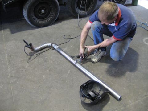 1978 Ford Bronco - A mechanic works on an exhaust pipe in a workshop, with a welding mask nearby.