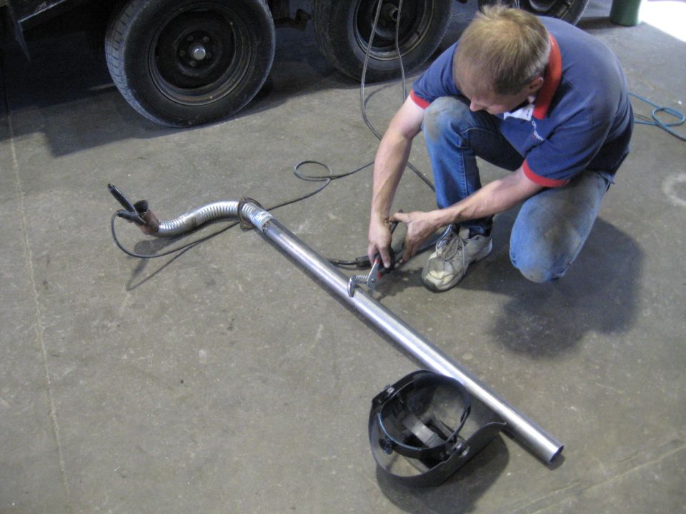 Man welding an exhaust pipe with a welding mask on the ground