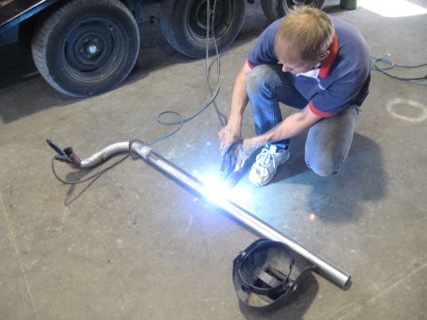 1978 Ford Bronco - A person is welding a car exhaust pipe, with a trailer in the background.