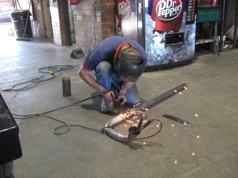 1978 Ford Bronco - Mechanic welds a section of exhaust pipe in a workshop environment.
