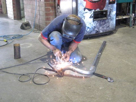 1978 Ford Bronco - A mechanic welds an exhaust pipe in a workshop, with sparks flying.