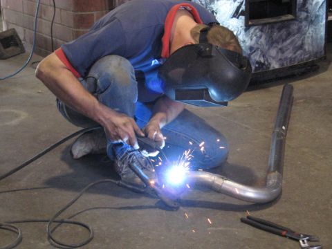 1978 Ford Bronco - A person is welding a section of exhaust pipe in a workshop environment.