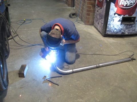 1978 Ford Bronco - A person is welding a section of exhaust pipe in a workshop setting.